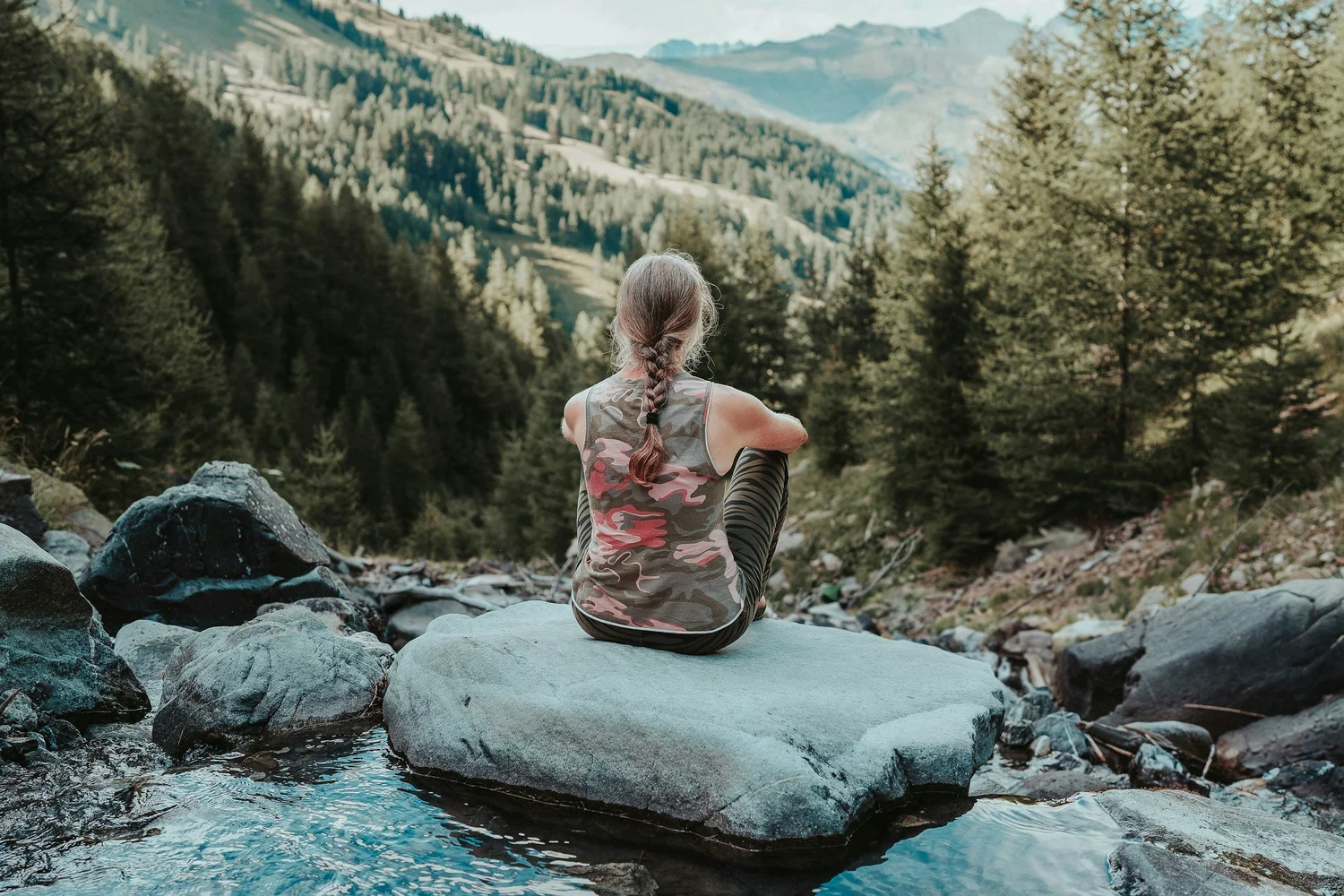 A woman sits on a rock overlooking a valley, feeling free